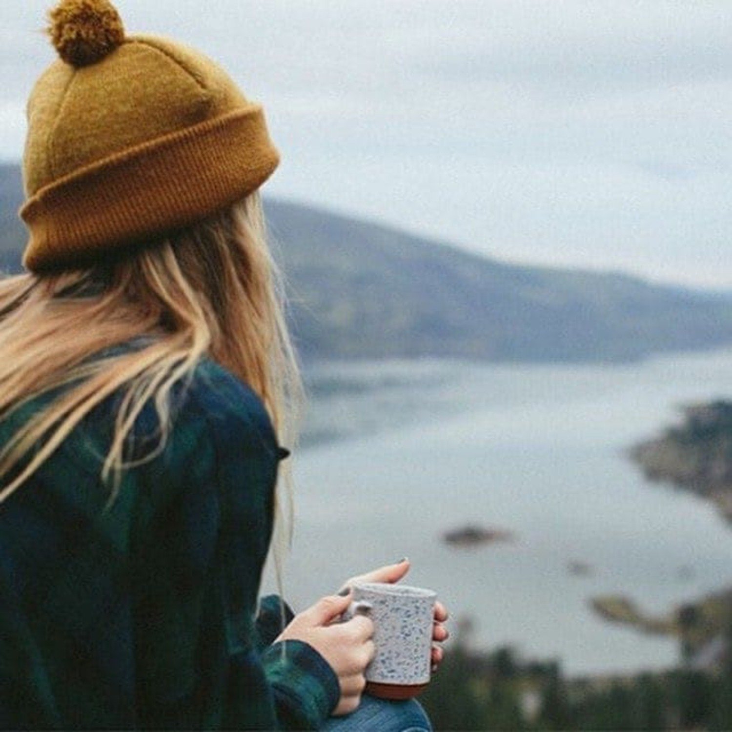femme bord fjords avec tasse de thé et bonnet jaune